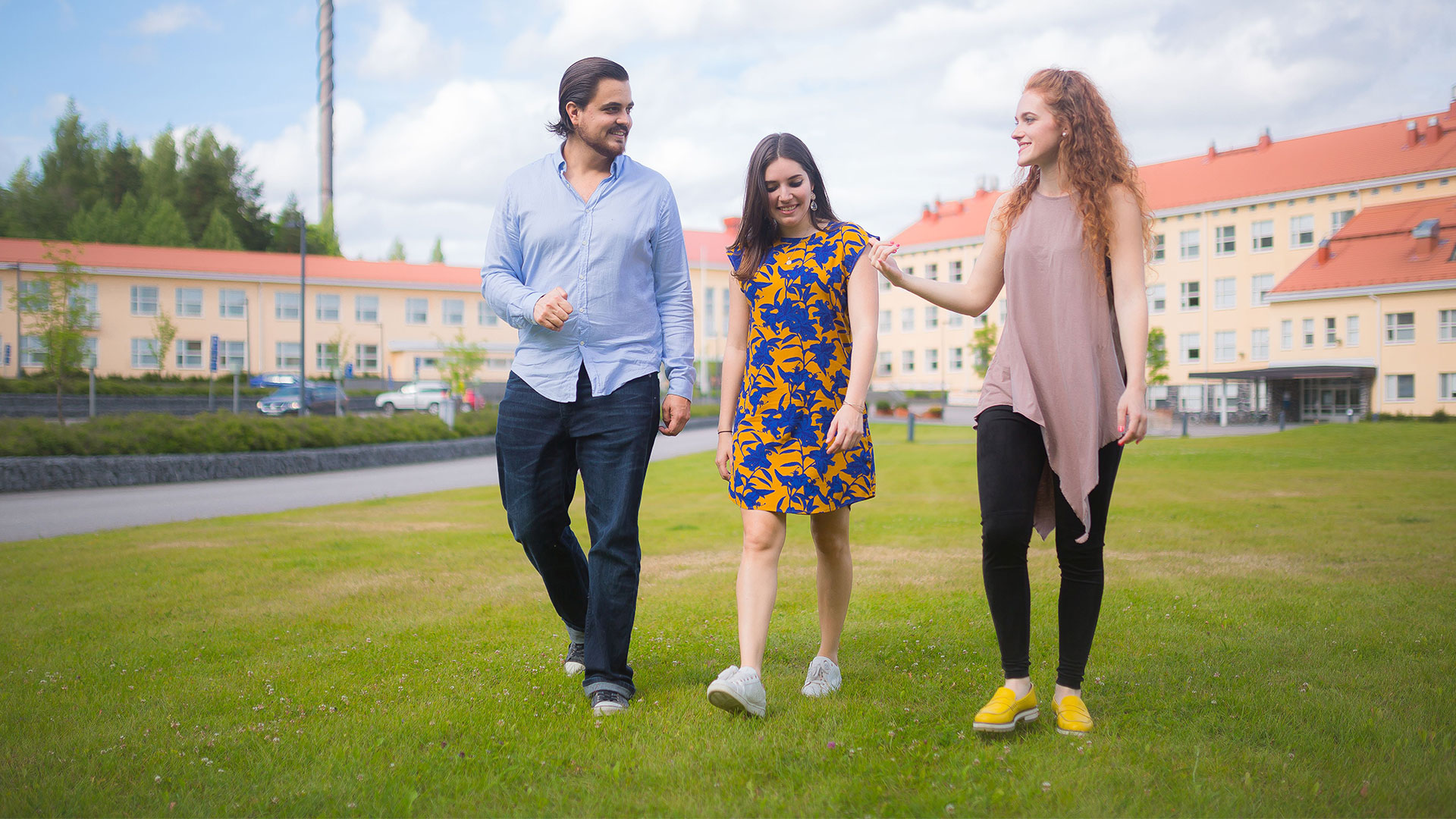 3 students walk in summer clothes in the main campus yard