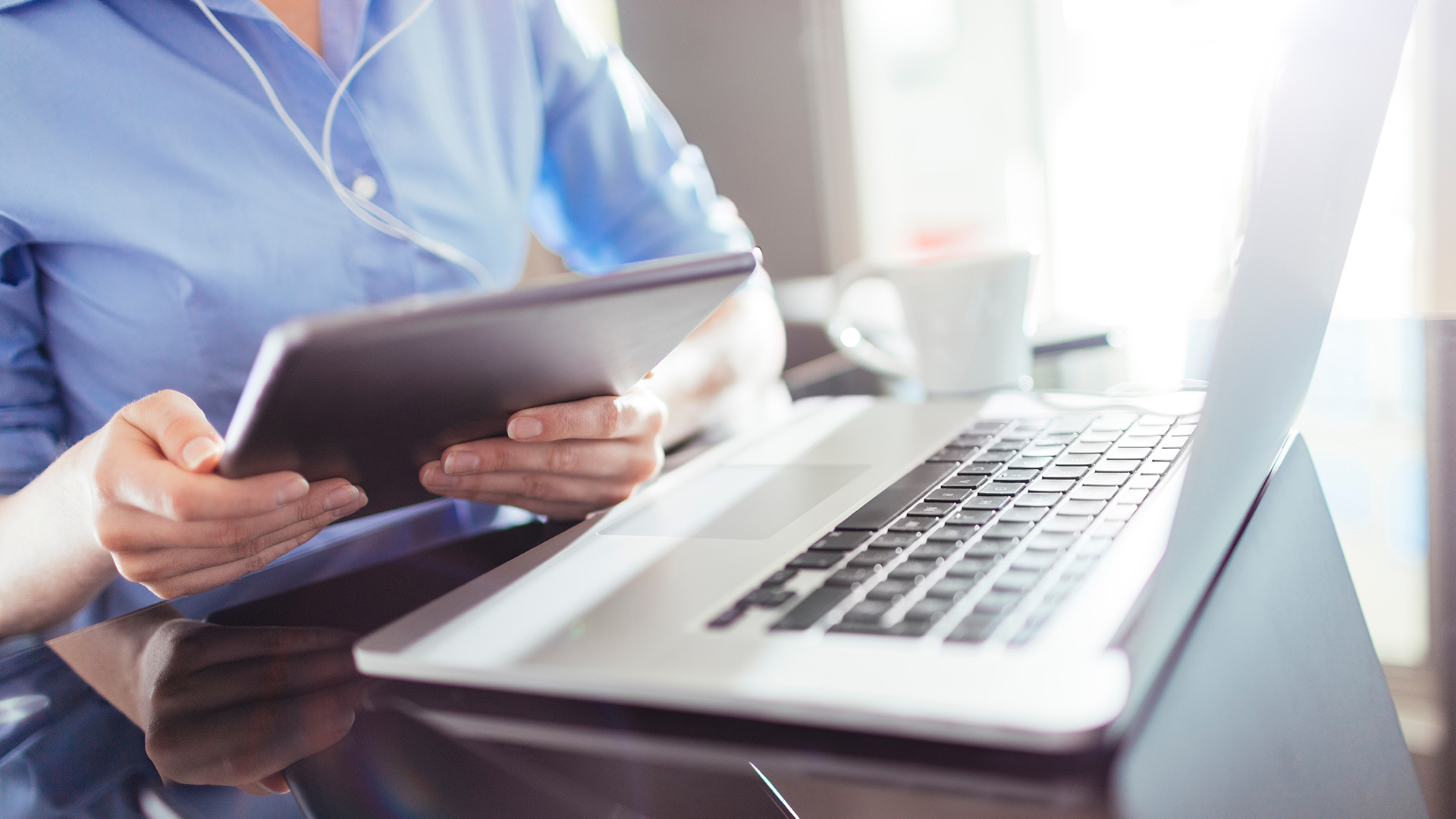 Closeup of person holding iPad and laptop on table