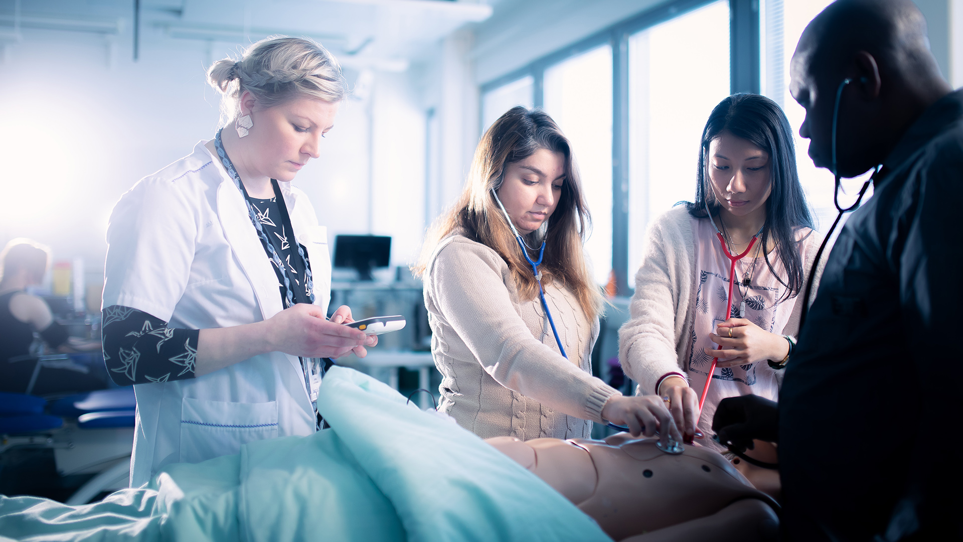 Students practising a nursing scenario with nursing manikin and teacher
