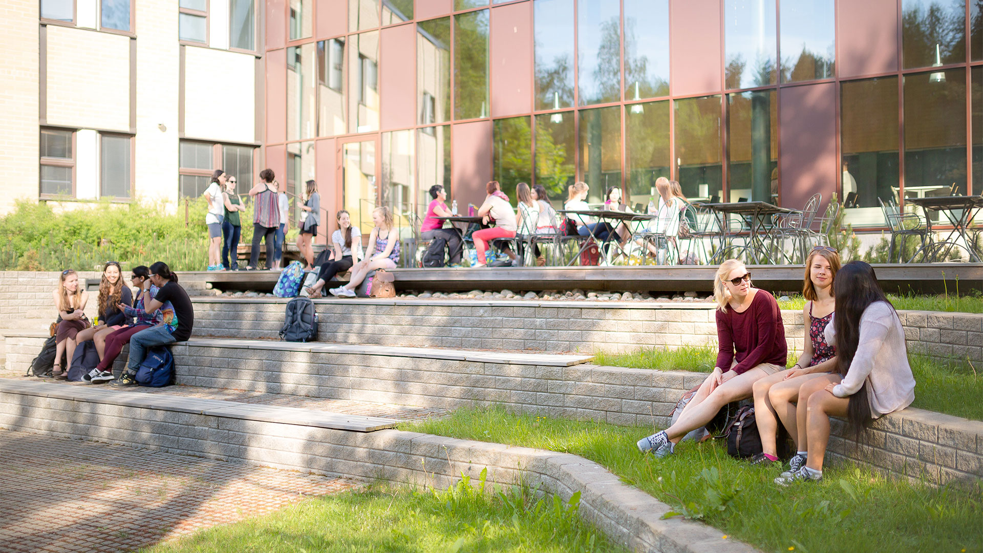 Students sit on music campus terrace. Building´s windows reflects trees and sky.