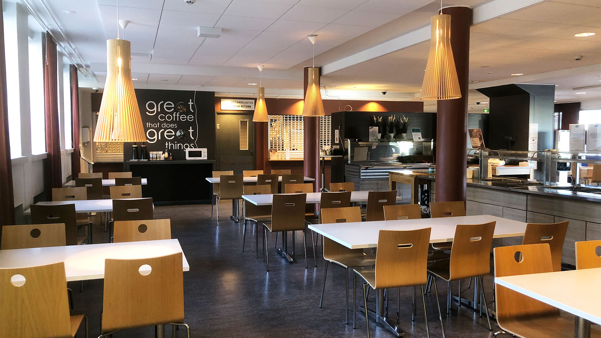 Kahvilassa pöytiä ja riippuvia valaisimia. Taustalla näkyy myyntitiski