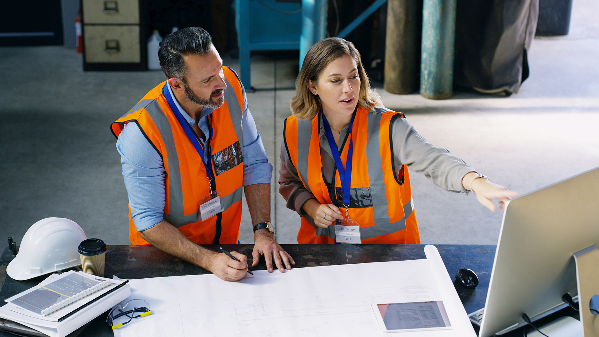 Kaksi suunnittelijaa huomioliiveissä tehdashallissa katsomassa tietokonetta