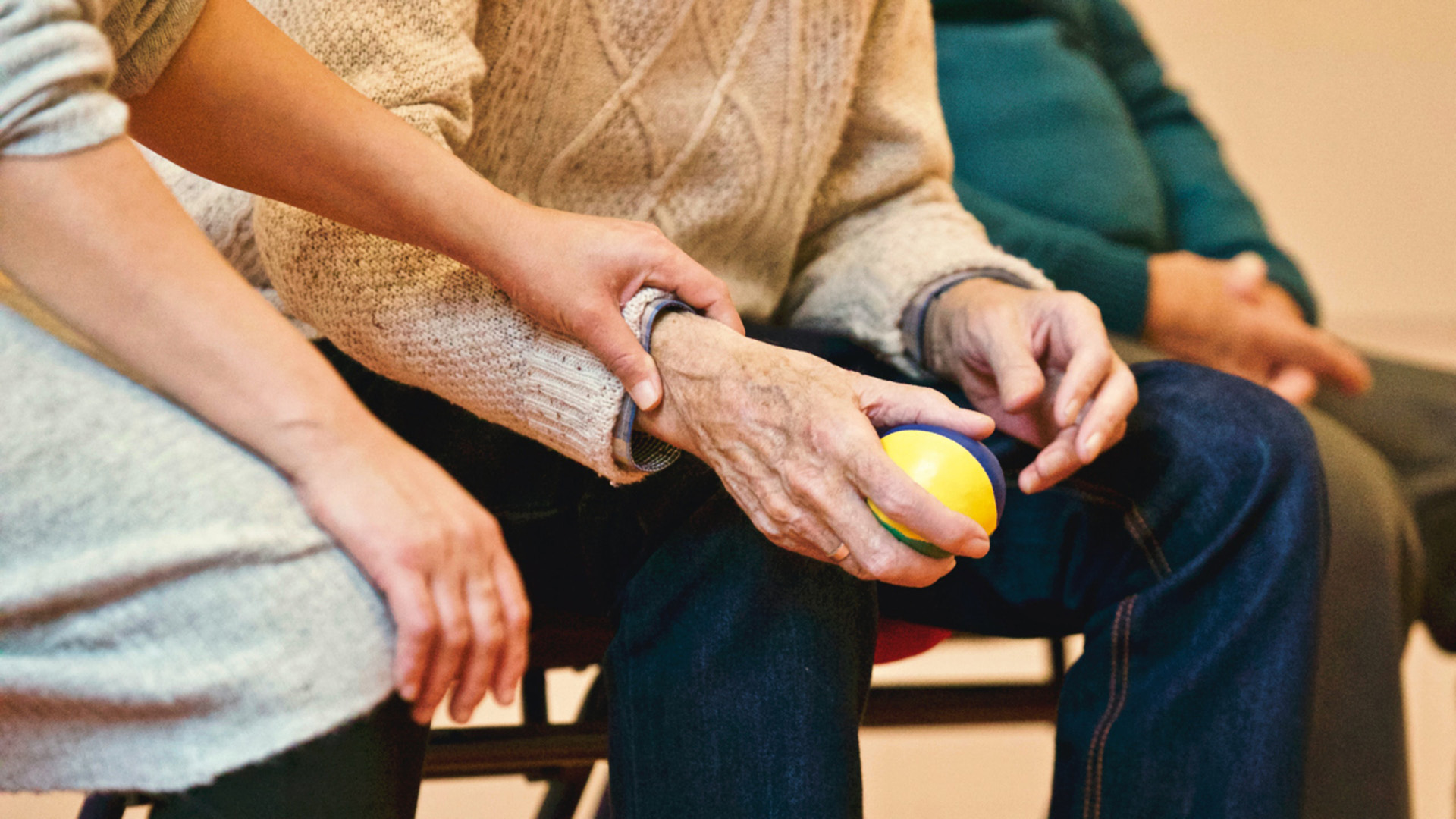 Seniori istuu ja ohjaaja pitelee kädestä