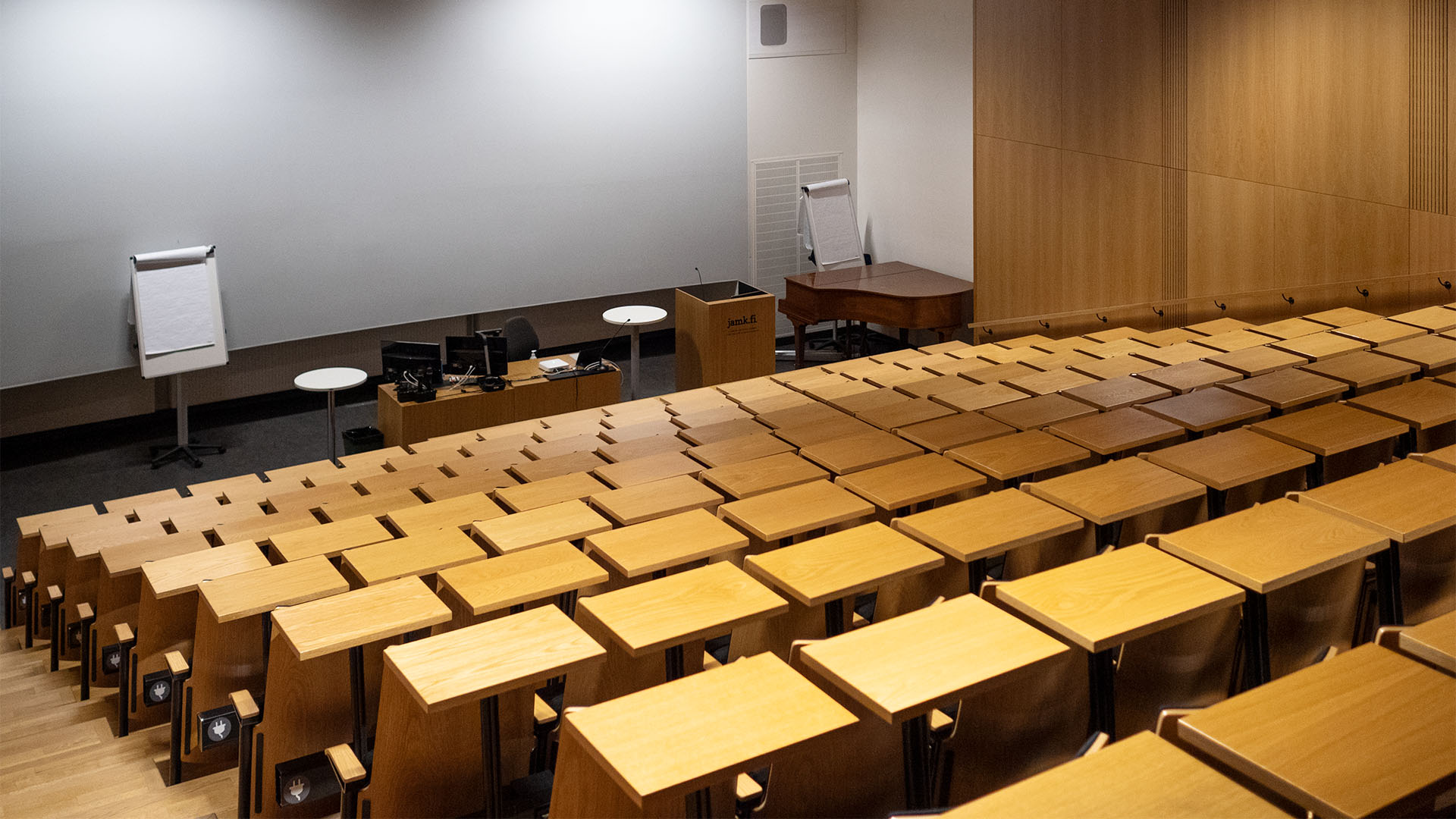 Auditorium above towards speakers desk. Wooden desks in a row