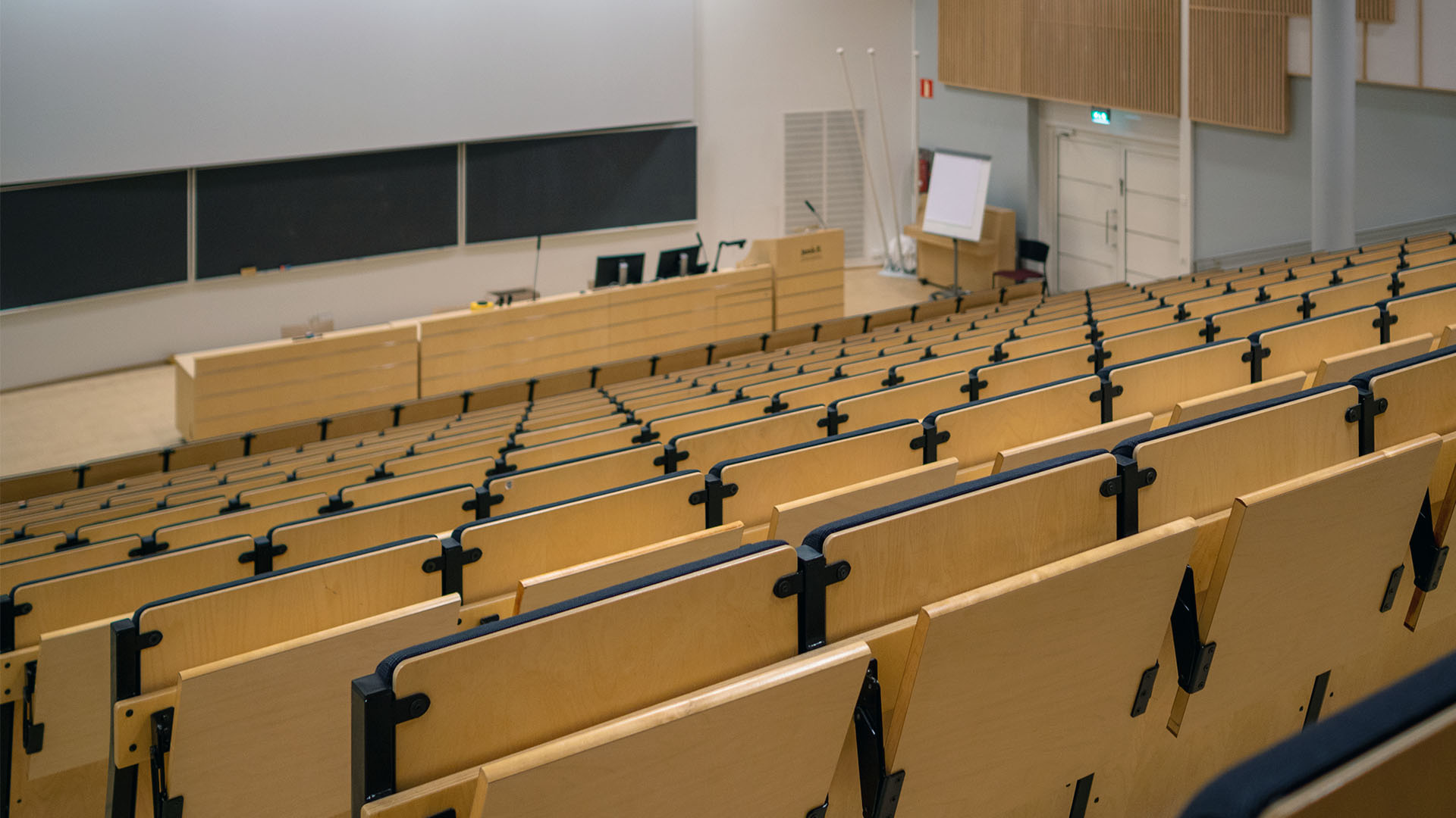 Auditorium above towards speakers desk. Wooden desks in a row
