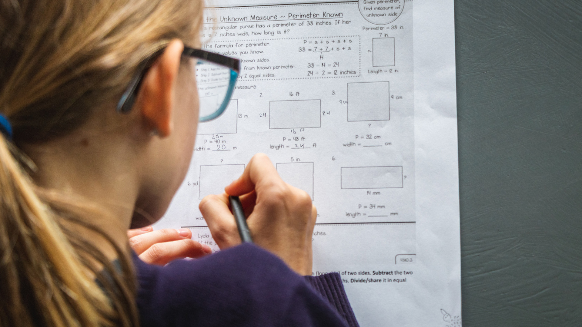 Peruskouluikäinen lapsi kirjoittaa seinällä olevaan paperiin matematiikan laskuja.