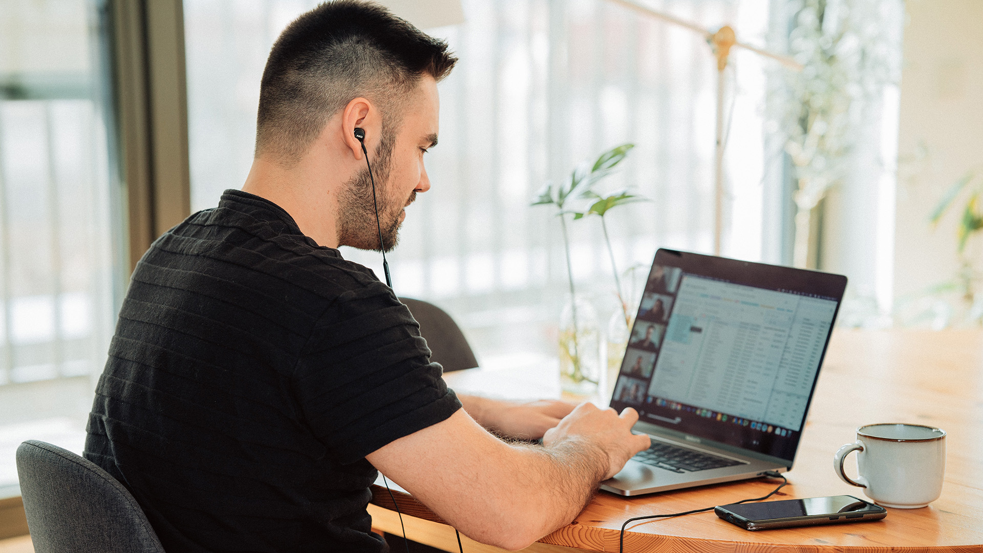 Mies istuu ja osallistuu läppärin ruudulla näkyvään verkkokokoukseen.