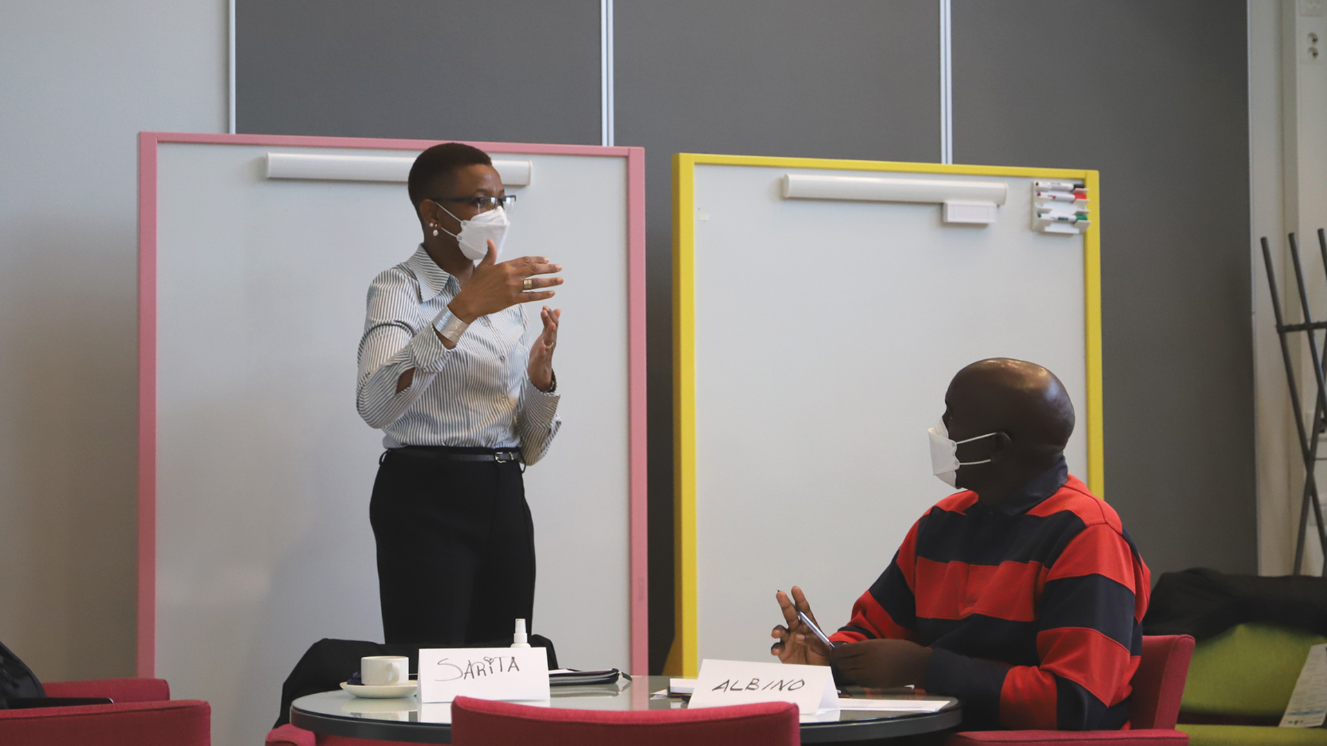Two teachers, wearing masks, discussing in front of a white board