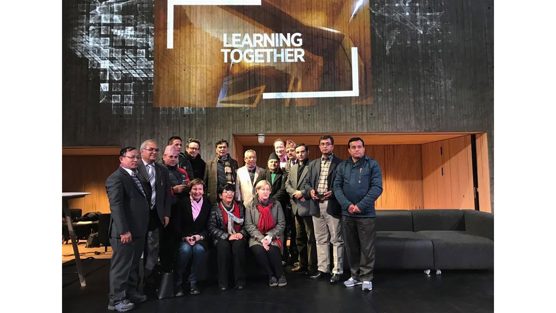 Project partners, 16 adults sitting and standing in front of a wall with text Learning together
