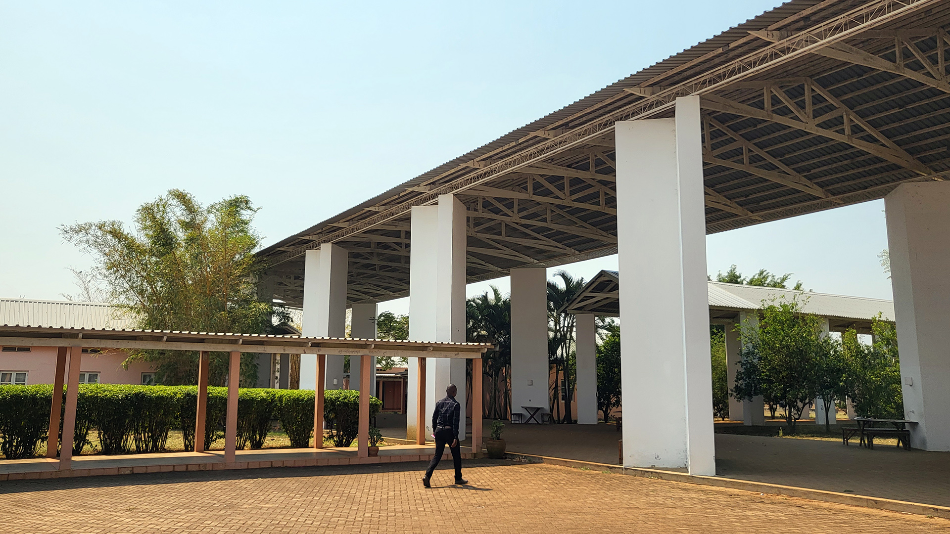 The ISET One-World school building from outside, with high roof. One man walking to the school.