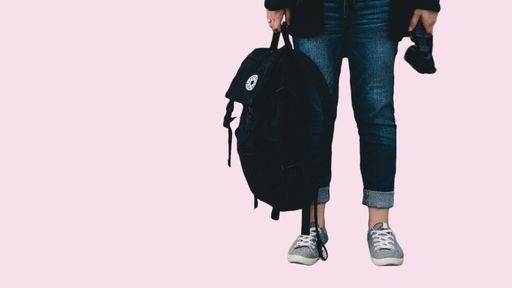 Henkilö seisoo ja pitää kädessään reppua.