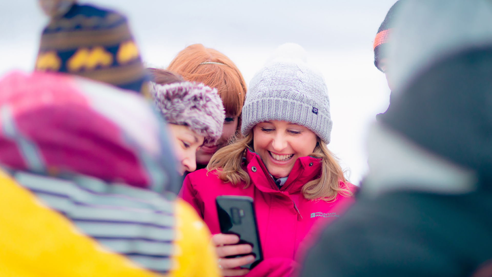 Talvivaatteisiin pukeutuneet opiskelijat katsovat puhelinta lumisessa maisemassa