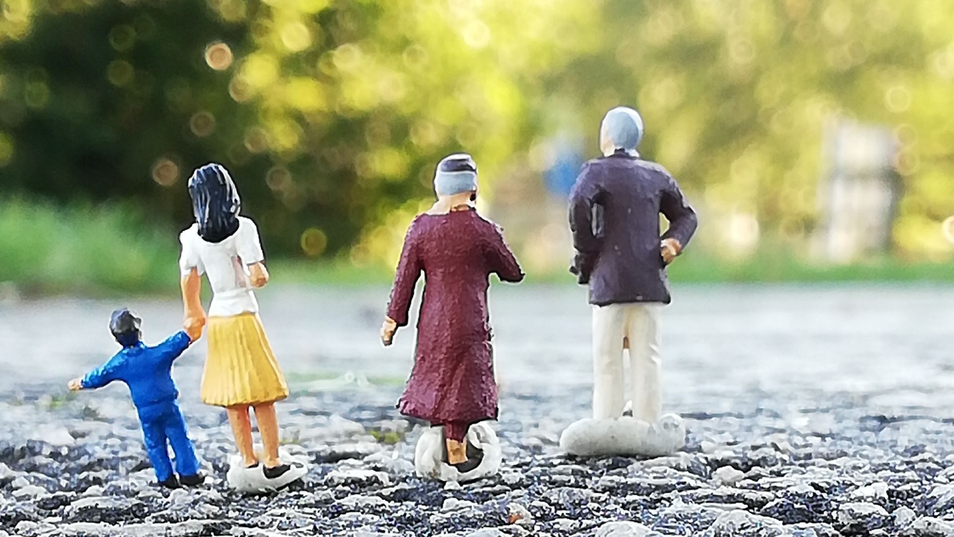 Neljä miniatyyrihahmoa seisovat rivissä asvaltilla ja taustalla on puita.