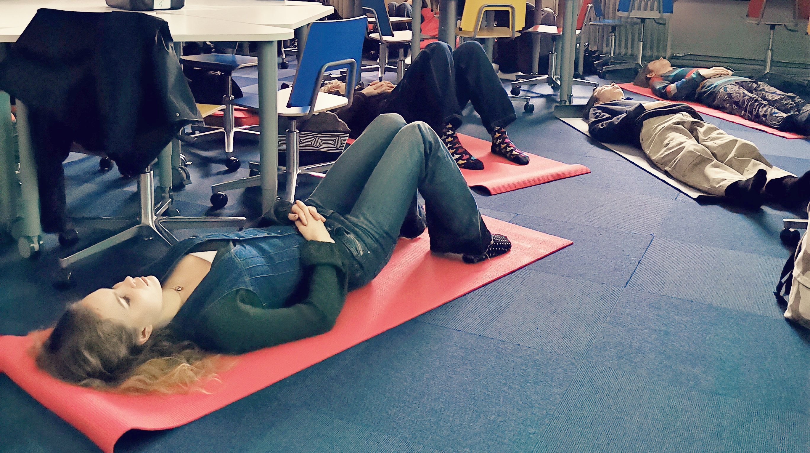 Opiskelijoita makaa luokkahuoneen lattialla joogamattojen päällä.