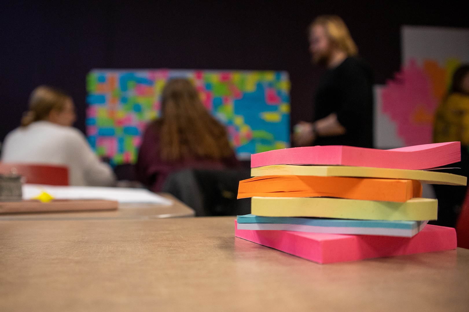 Kuvassa post-it lappuja ja taustalla työskentelevä ryhmä