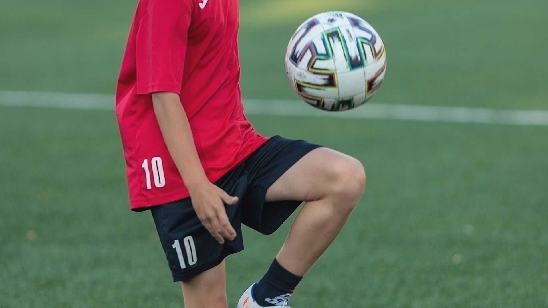 Lapsi pompottaa polvellaan jalkapalloa.