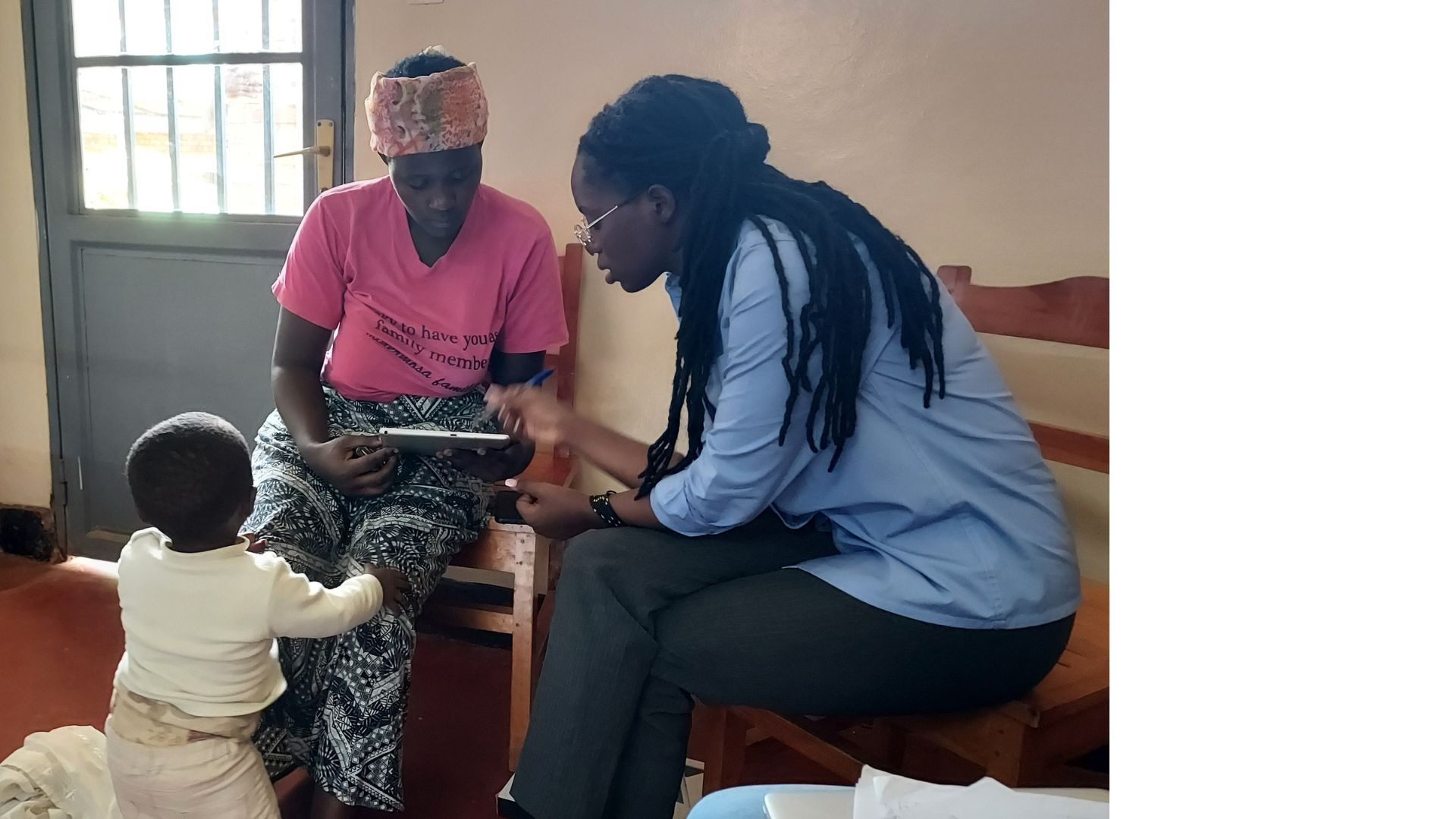 Mother with a child in ward with rehabilitation professional showing a digital device