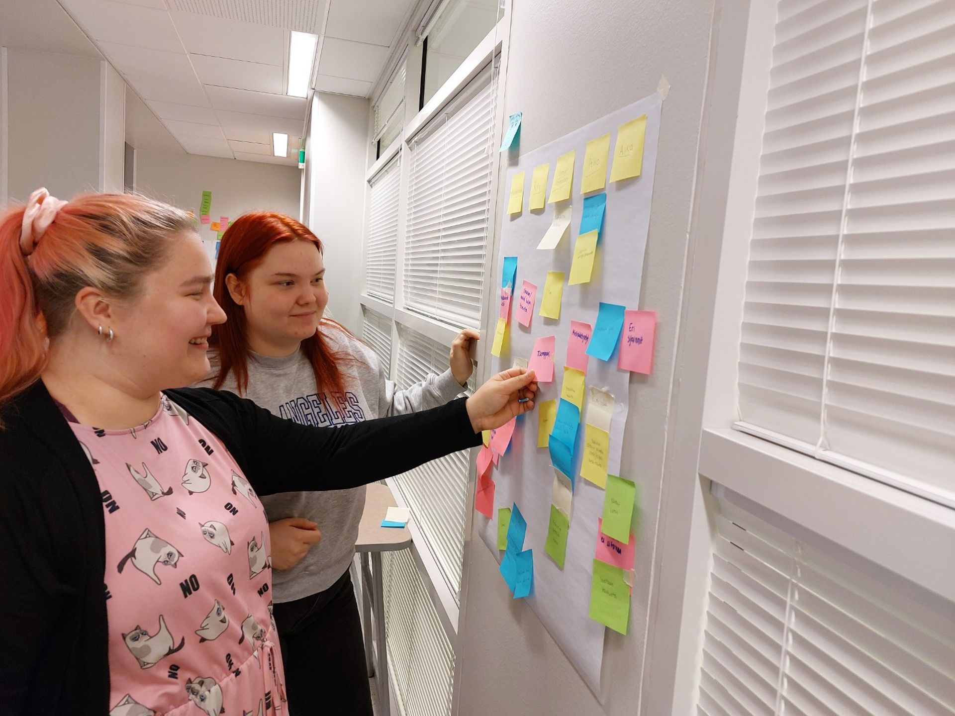 Suvi Siekkinen ja Veera Marttinen katsovat seinällä olevia post it -lappuja.