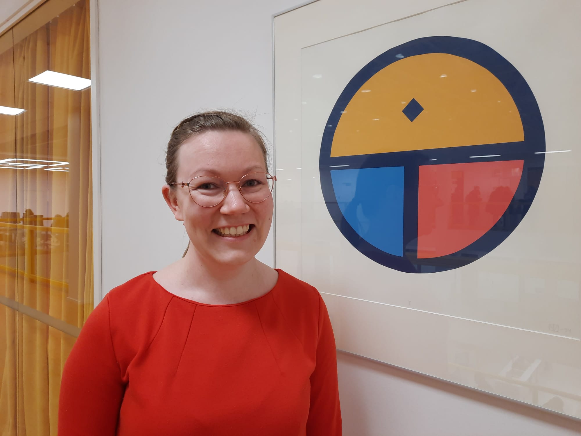 Kuvassa opiskelija Heidi hymyilee ja seisoo taulun vieressä