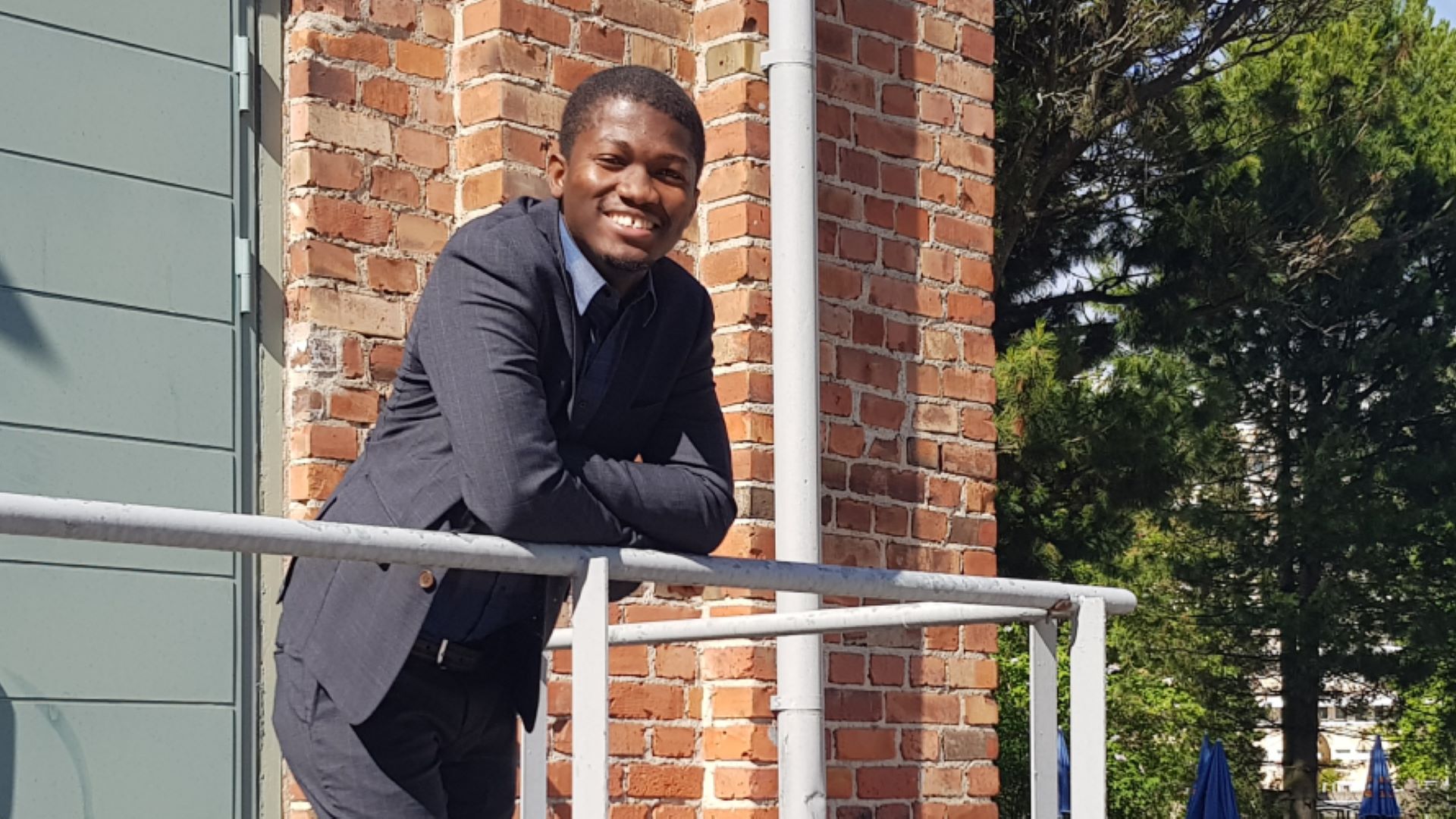 Sulaymon Tajudeen seisoo aurinkoisella terassilla punatiilisen talon edessä ja hymyilee.