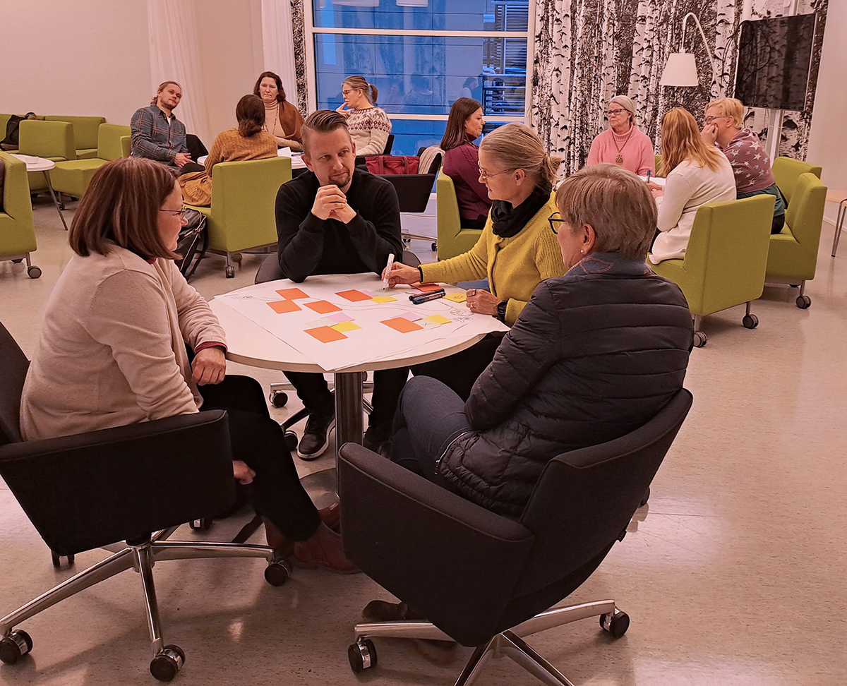 Joukko ihmisiä tekee ryhmätöitä pyöreiden pöytien ympärillä