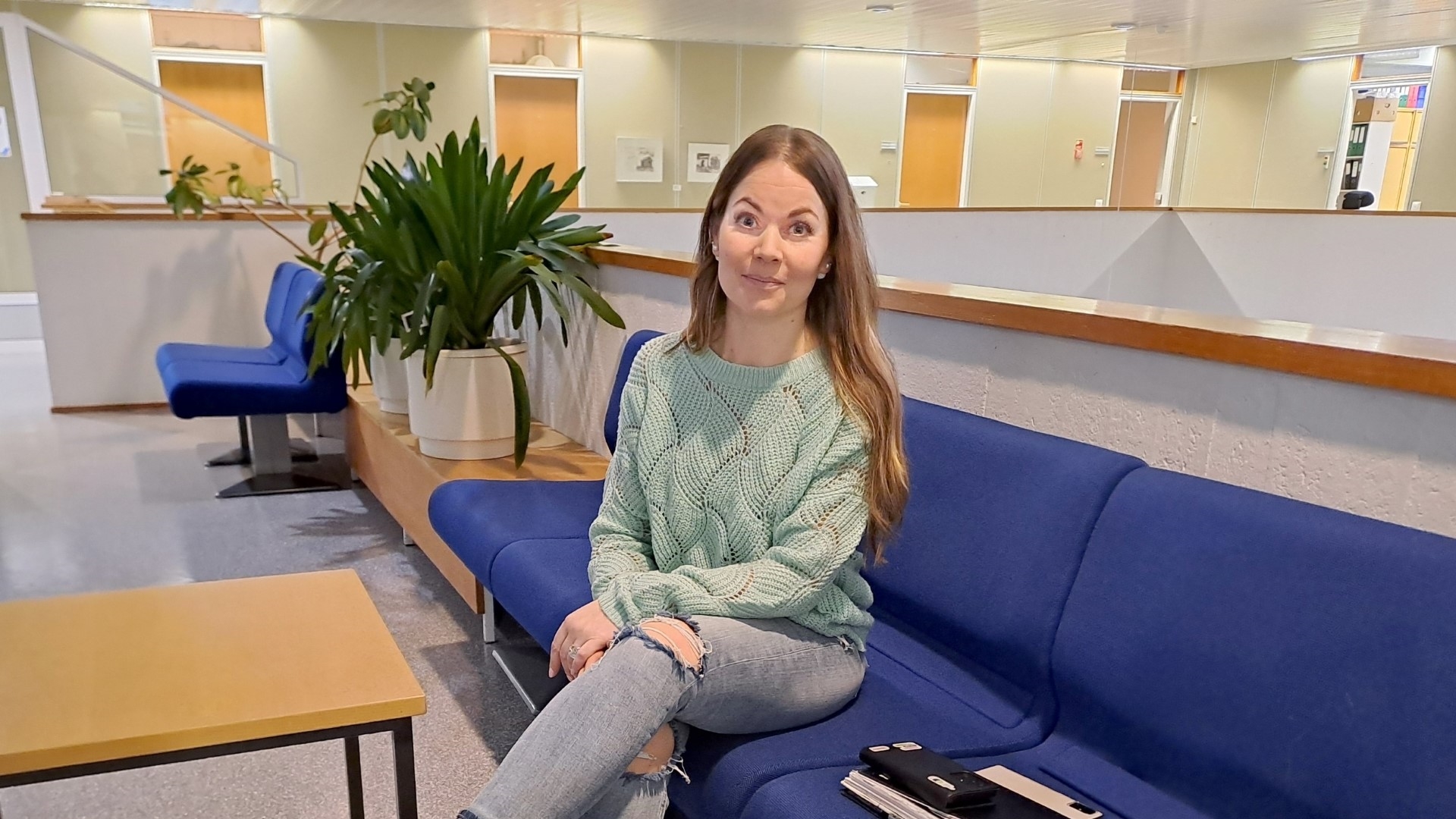 Sini Heinonen istuu sinisellä sohvalla ja katsoo hymyillen suoraan kameraan.