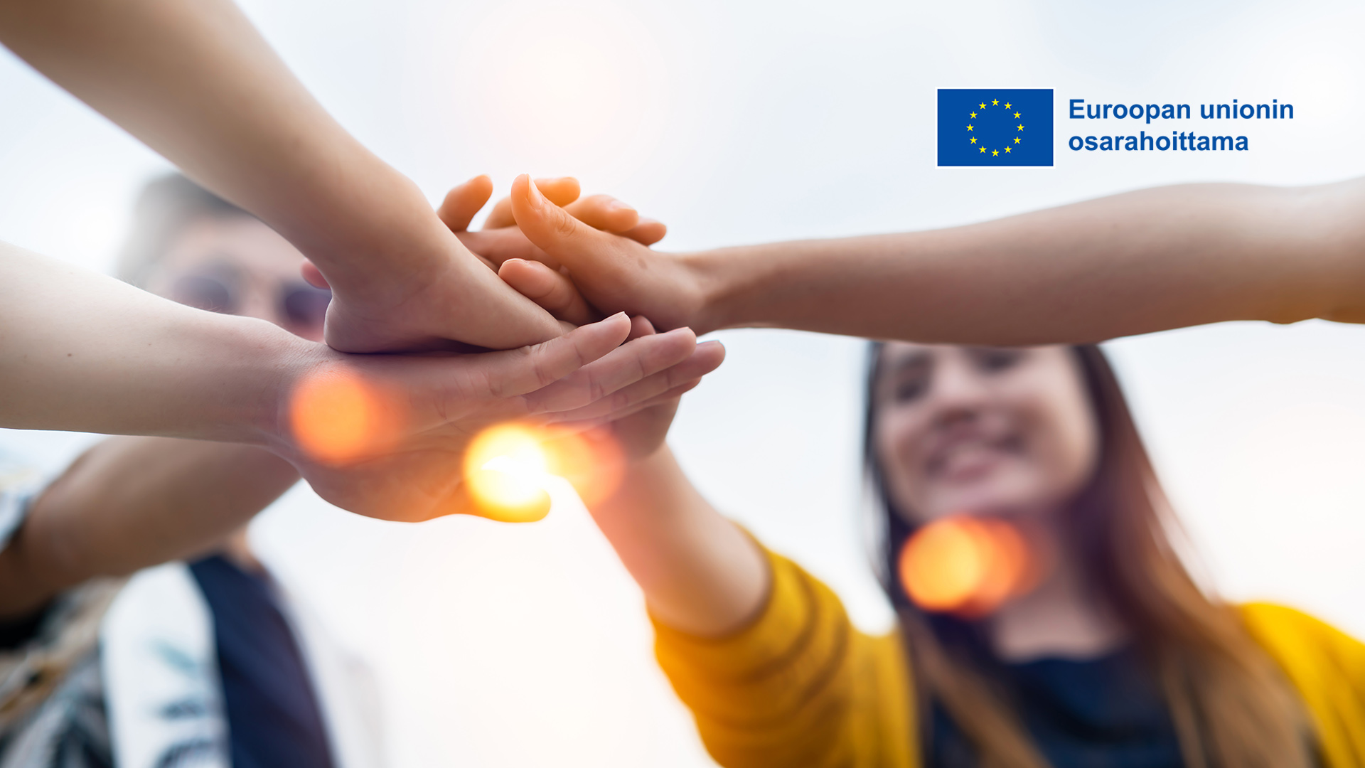 Ryhmä hymyileviä nuoria pitää käsiä pinossa, Euroopan unionin osarahoittama -logo