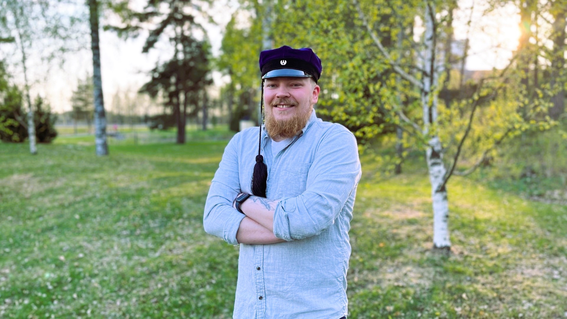 jere Hirvonen seisoo keväisessä luonnossa ja hymyilee kameraan. Hänellä on insinöörilakki päässään.