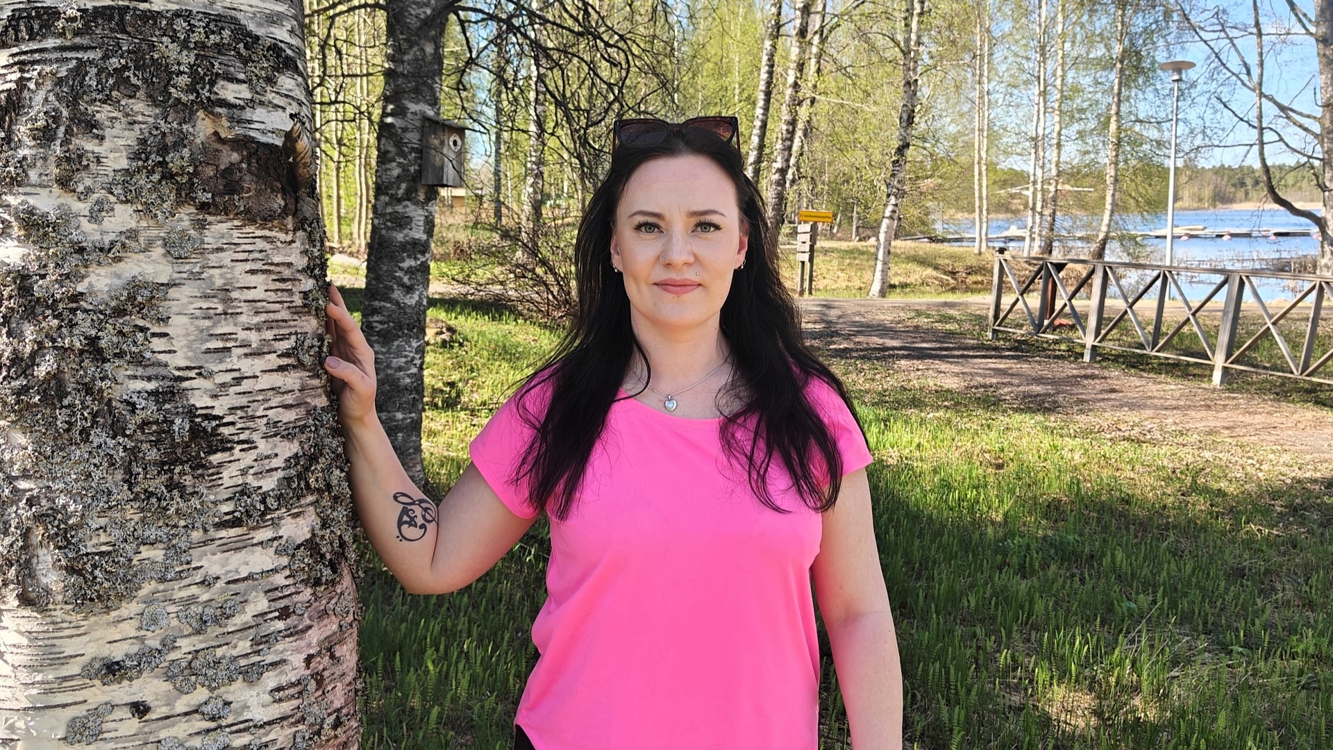 Petra nojaa oikella kädellään koivuun ja katsoo suoraan kameraan