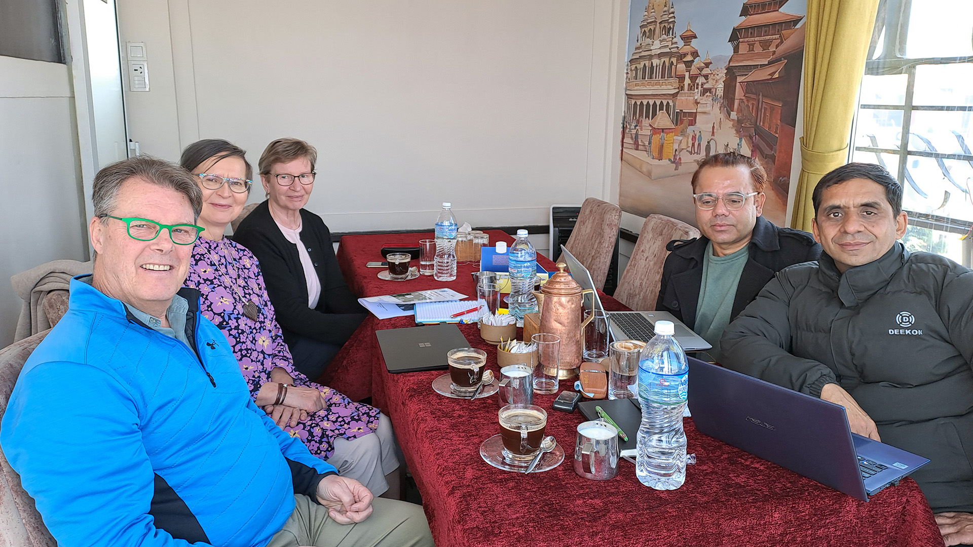 People sitting by a table in a meeting, with tea and coffee cups in front of them.