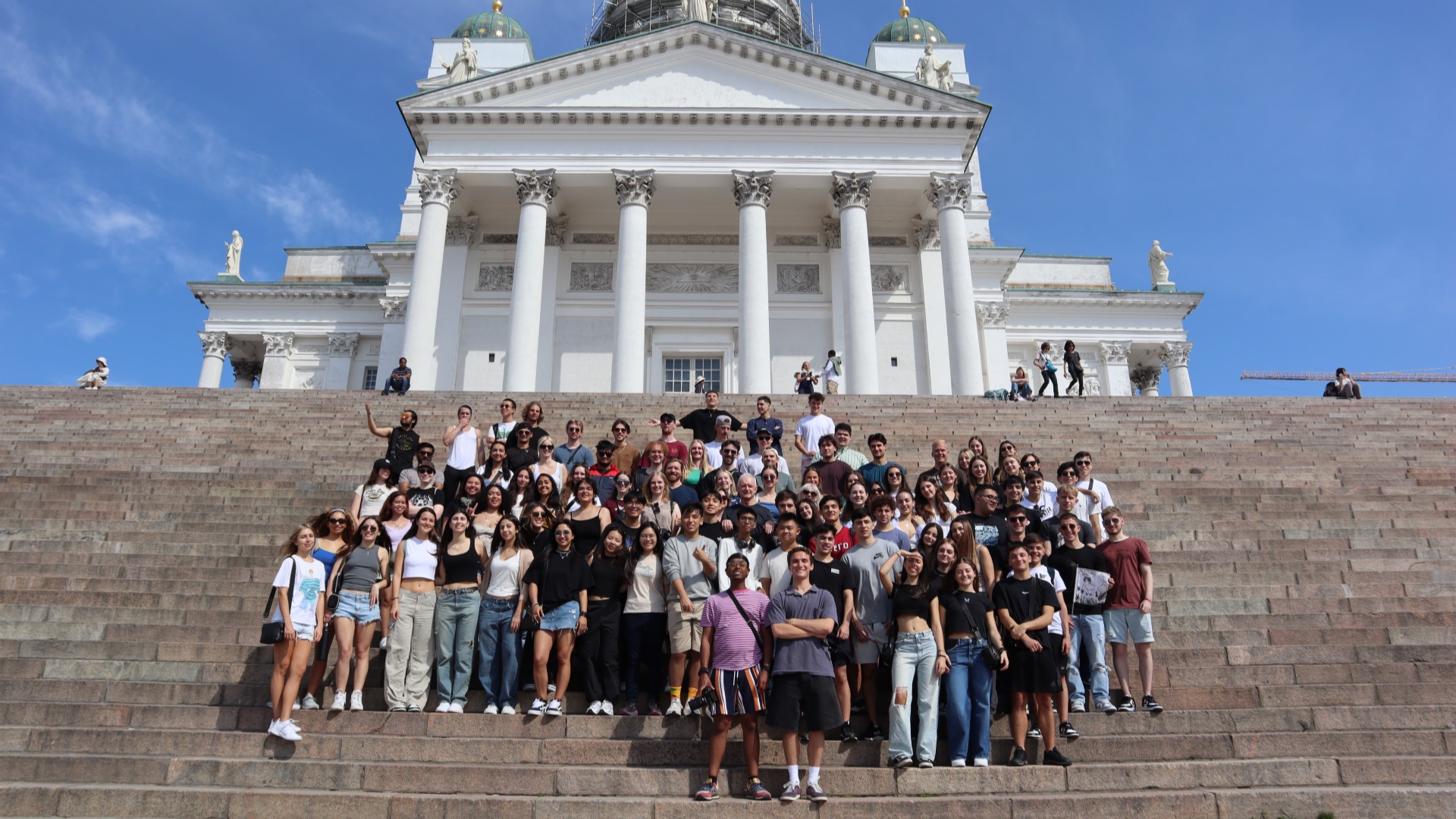 Summer School in Leadership students standing on the chairs leading to Helsinki Cathedral, smiling at the camera