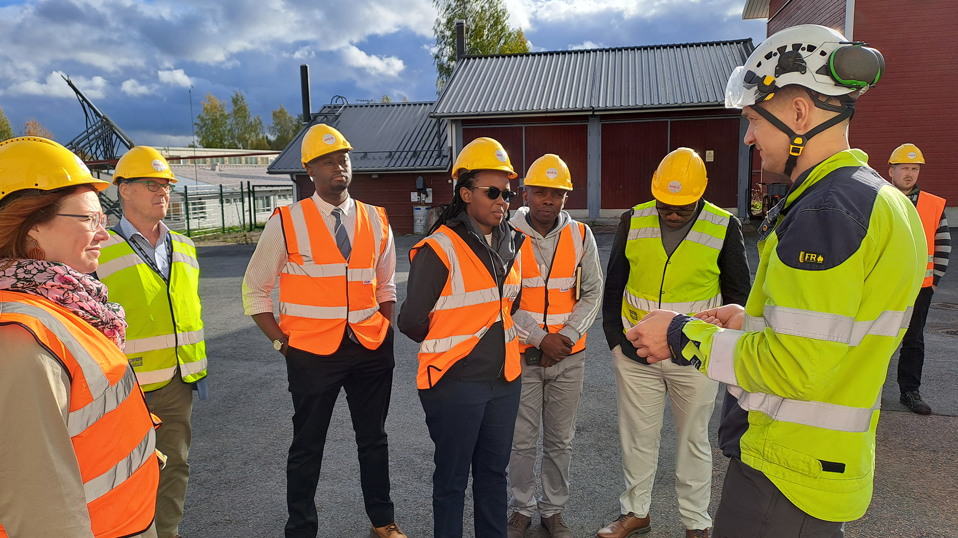 people wearing safety vests and helmets, near agricultural buildings