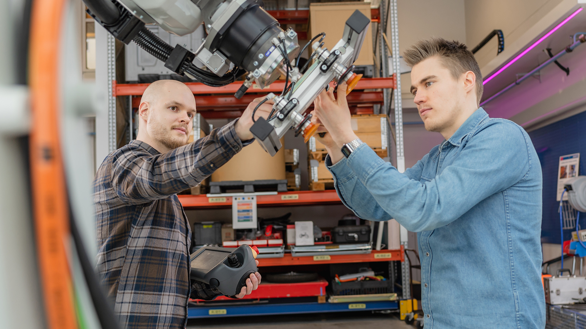 Kaksi miestä tutkii robotin tarttumakouraa hallissa