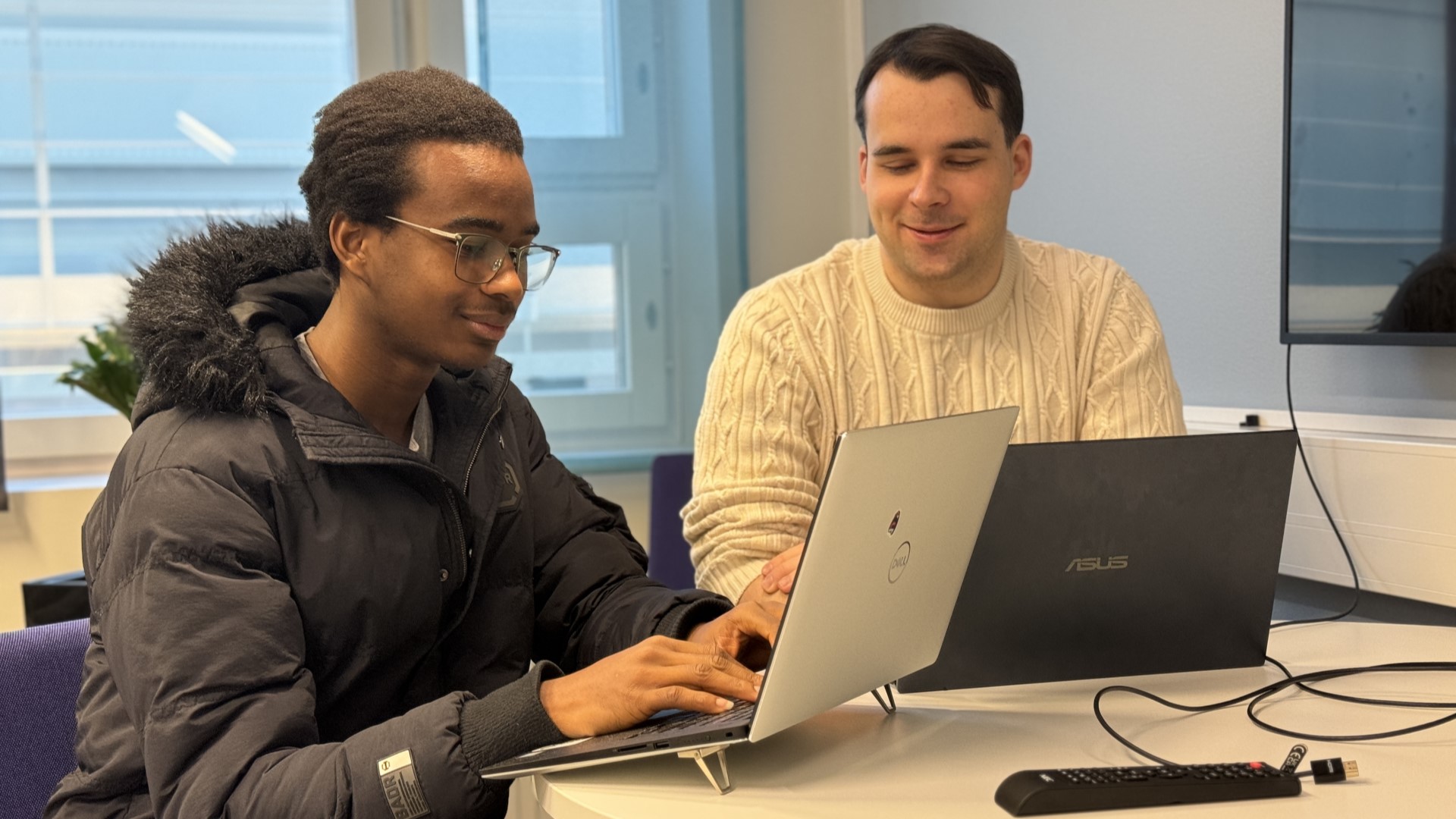 Two people working with computers in co-operation, focusing mainly on one screen.