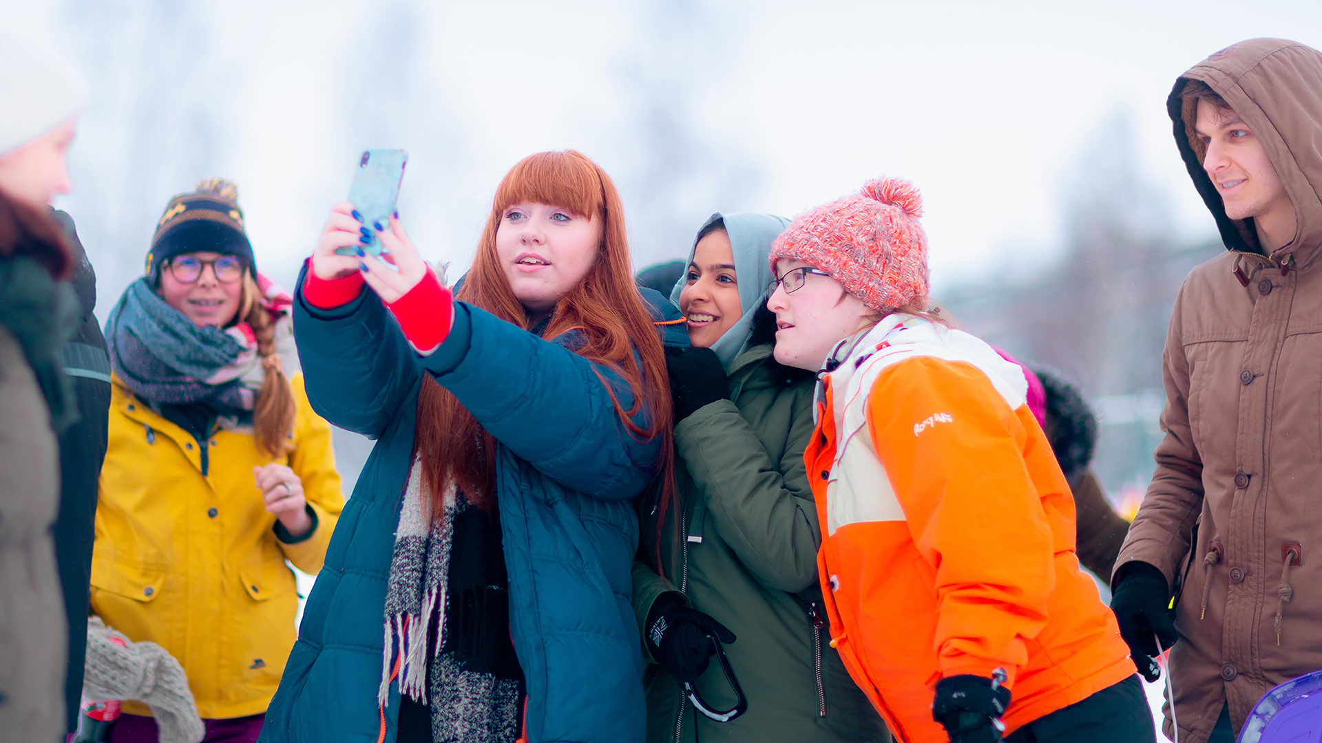 Ulkovaatteissa olevat opiskelijat ottavat ryhmäselfiekuvaa ulkona lumisessa maisemassa.