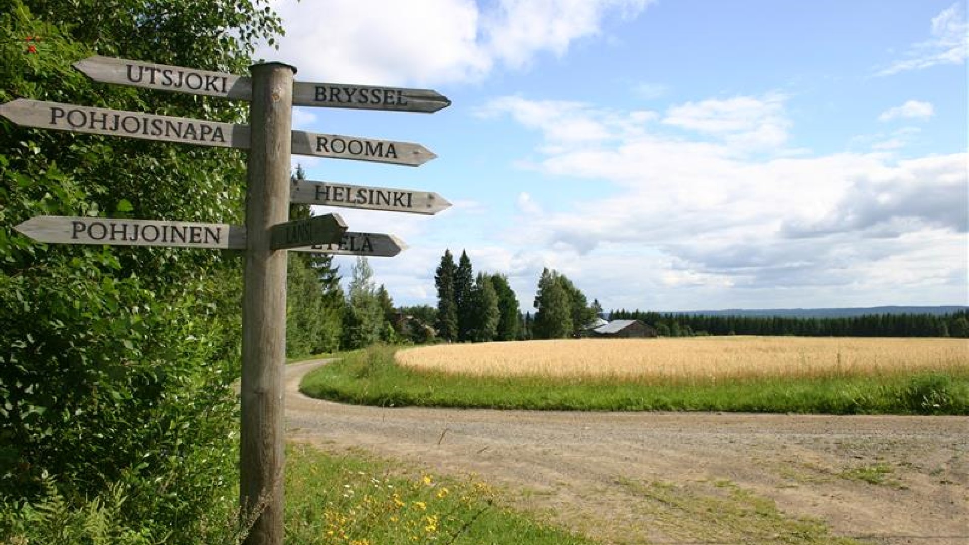 Kellertävää peltoa vasten oleva risteys, jossa vanhanaikainen puuopaste osoittaa humoristisesti niin eri ilmansuuntiin, Suomen pohjoisimpaan ja eteläisimpään kaupunkiin, kuin suuriin eurooppalaisiin kaupunkeihin.