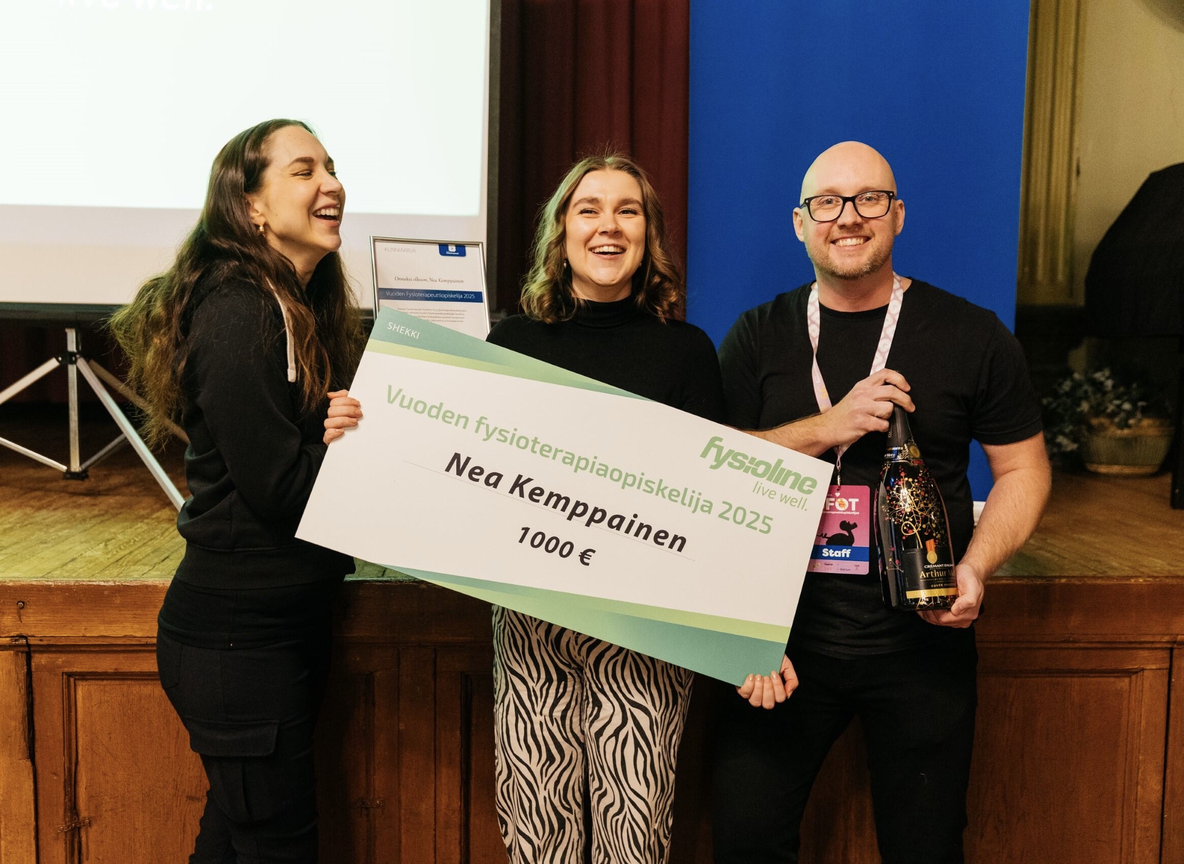 Kolme henkilöä, joista keskimmäisellä kädessä iso stipendikyltti, vuoden fysioterapeuttiopiskelija.