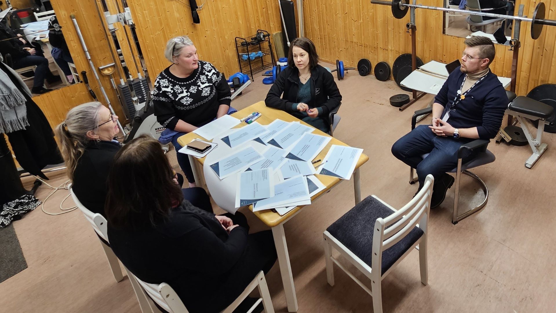 Viisi henkilöä keskustelemassa pöydän ääressä.