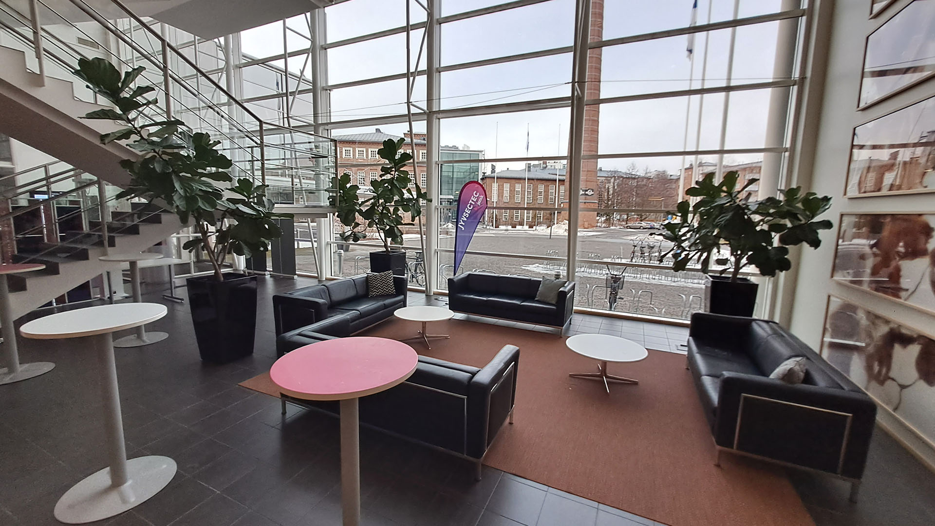 Big windows, black leather sofas, tables, pink rug, plants and stairs