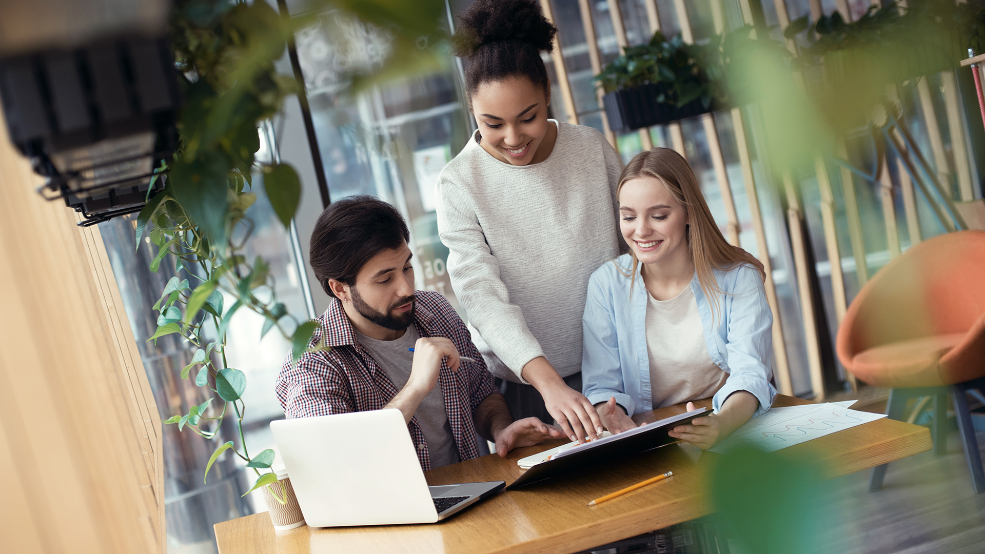 Kolme henkilöä työskentelee iloisina pöydän äärellä.