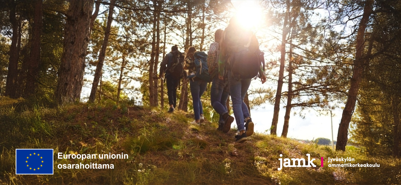 Joukko ihmisiä kävelee jonossa metsäisessä rinteessä polulla ja puiden välistä paistaa aurinko.