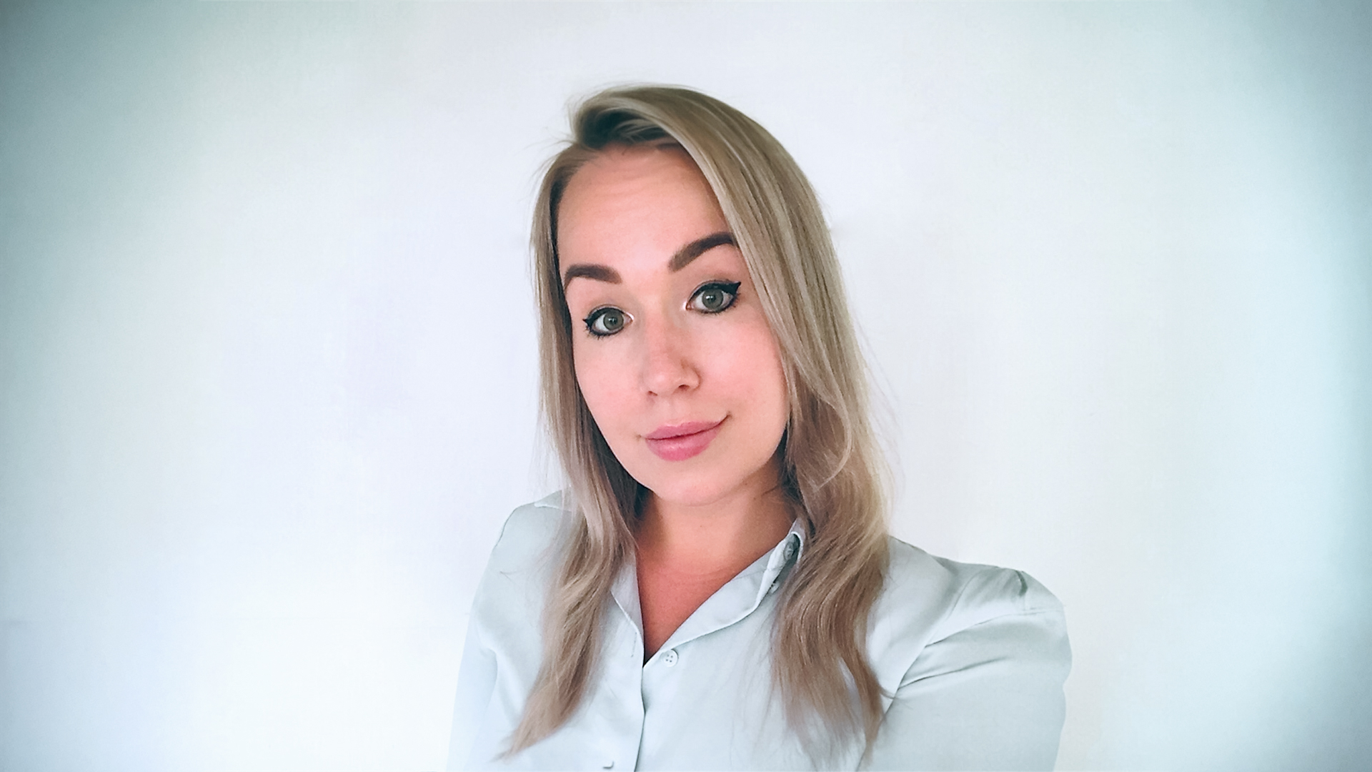 Smiling woman in the middle of the picture with gray background behind her.