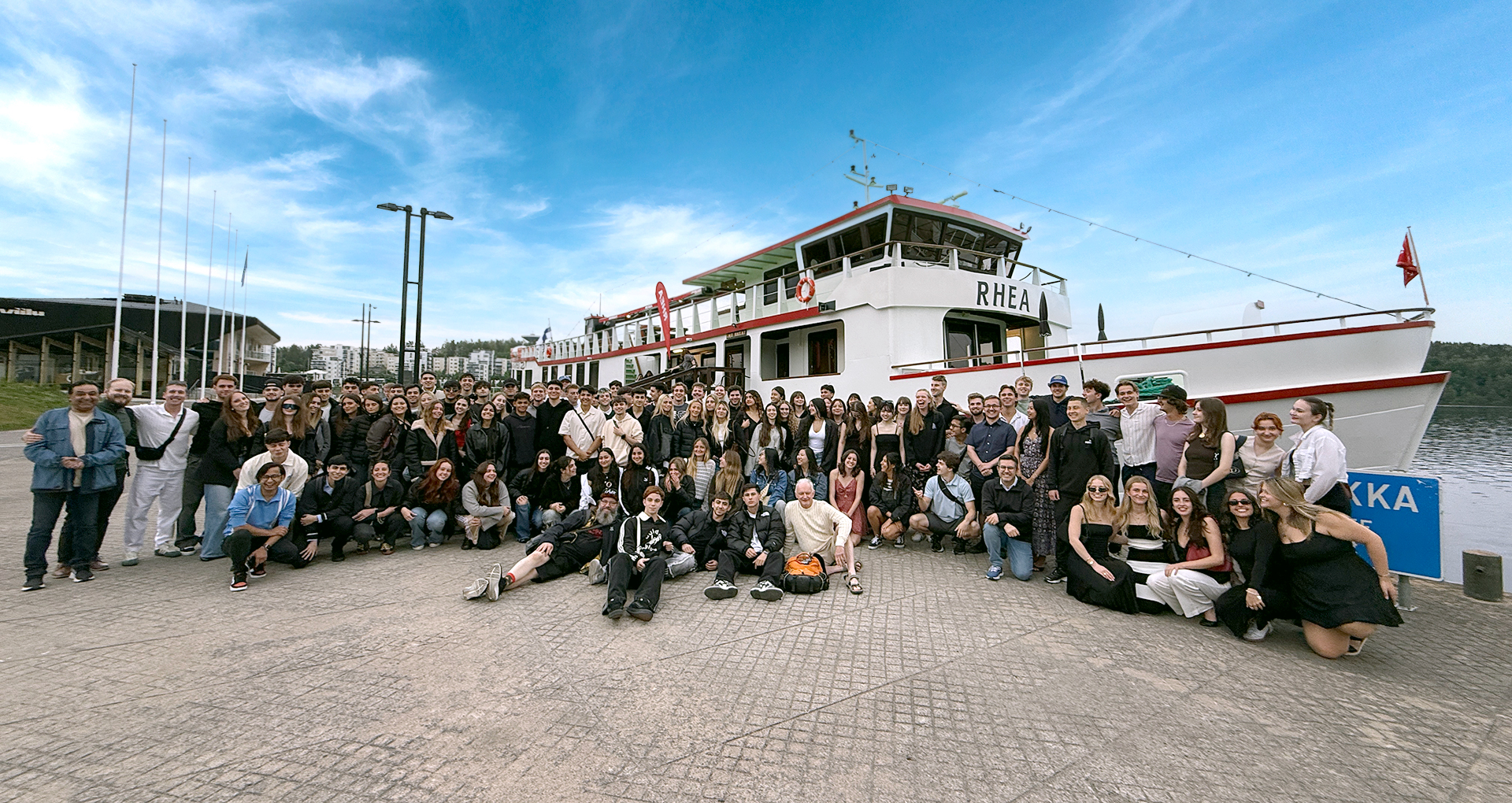 Happy group of people in harbour, posing in front of a big boat on a beautiful summer day.