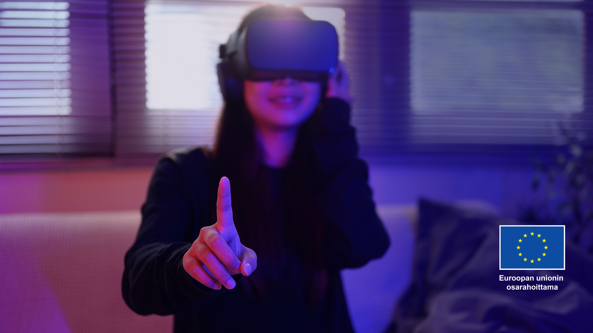 Nuori henkilö kohottaa oikean käden etusormensa käyttäessään virtuaalilaseja hämärässä huoneessa.