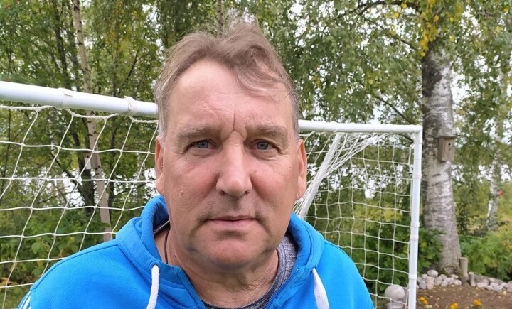 Henkilökuva miehestä sinisessä hupparissa. Taustalla jalkapallomaali.