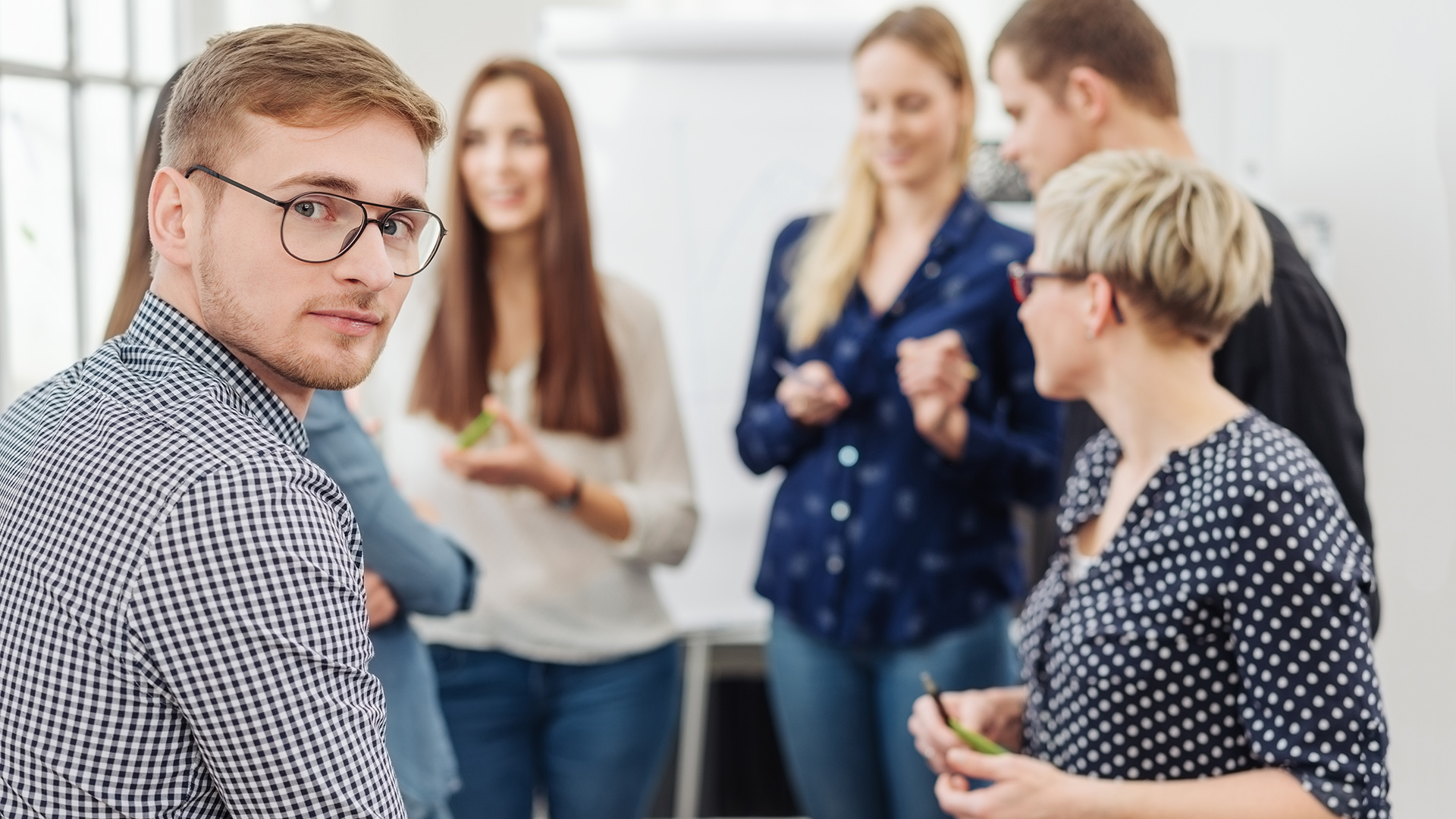 Ryhmä eri ikäisiä opettajia keskustelee taustalla ja yksi henkilö katsoo kuvaajaan.