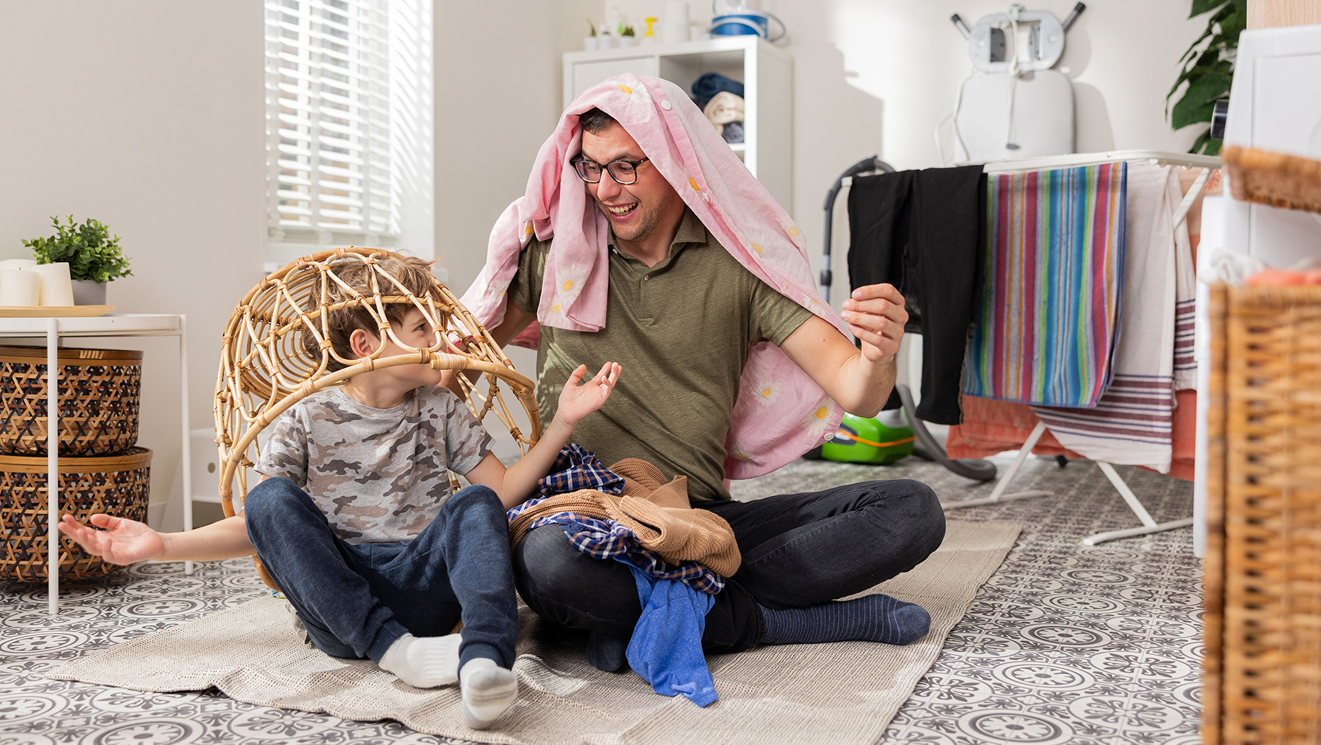 Mies ja lapsi leikkivät pyykkikorin alla.