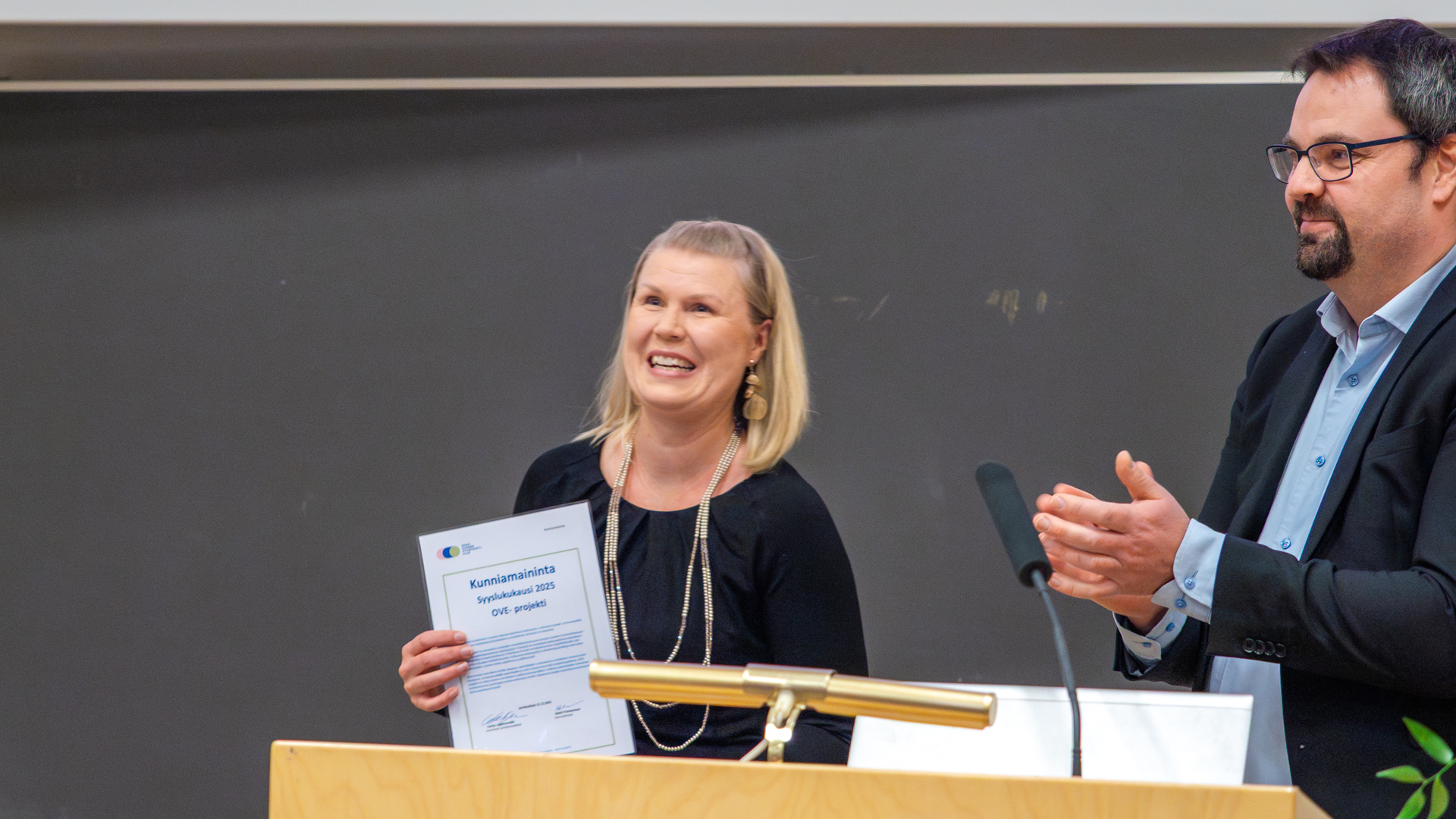 Naishenkilö pitelemässä hymyillen kunniakirjaa.