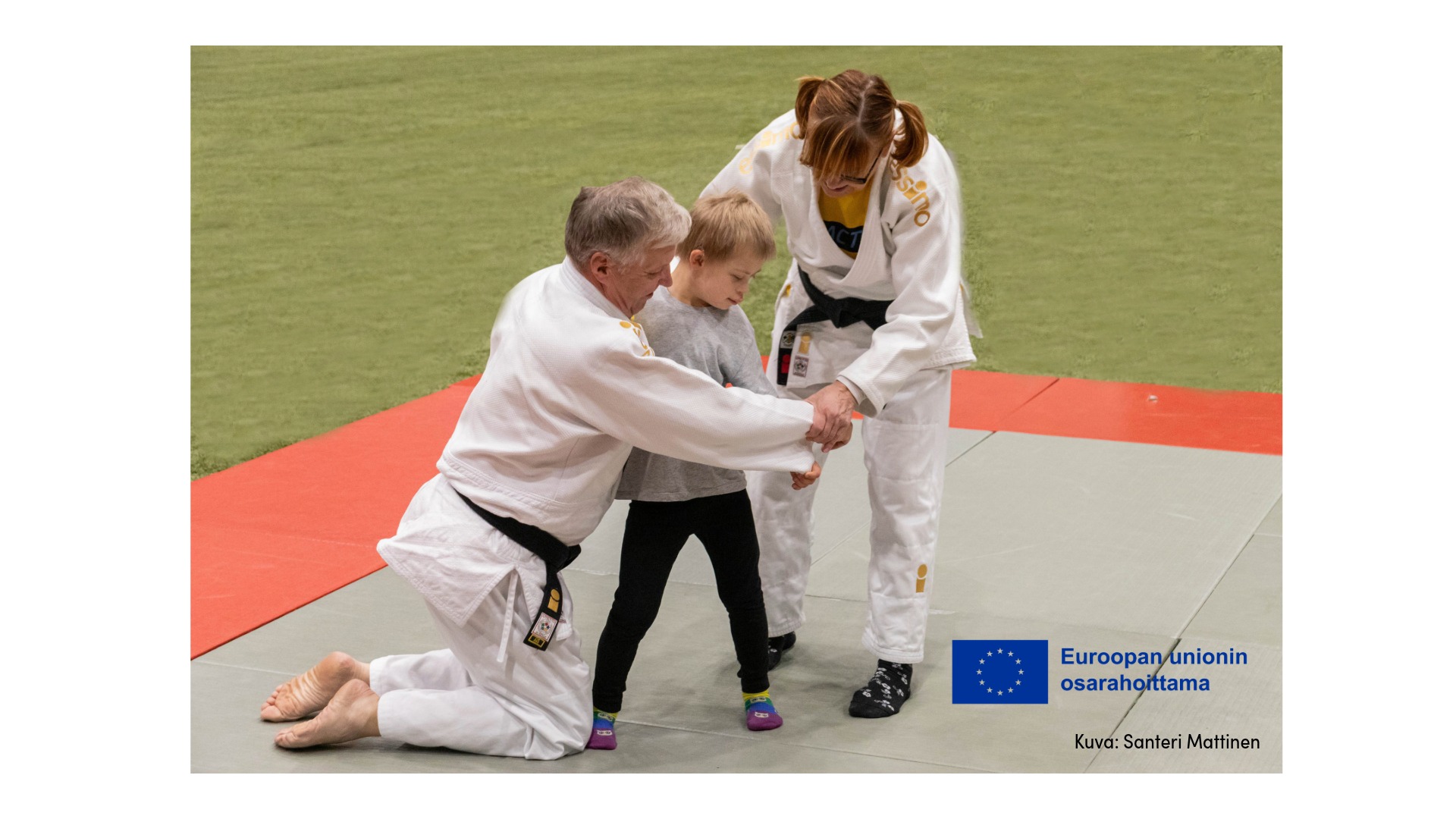 Kaksi aikuista opettaa lasta judoliikkeeseen.