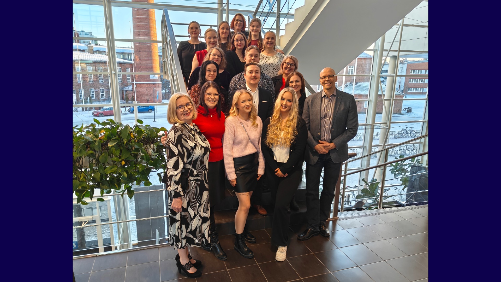 ryhmä hymyileviä ihmisiä, opiskelijoita ja lehtoreita, rappusissa